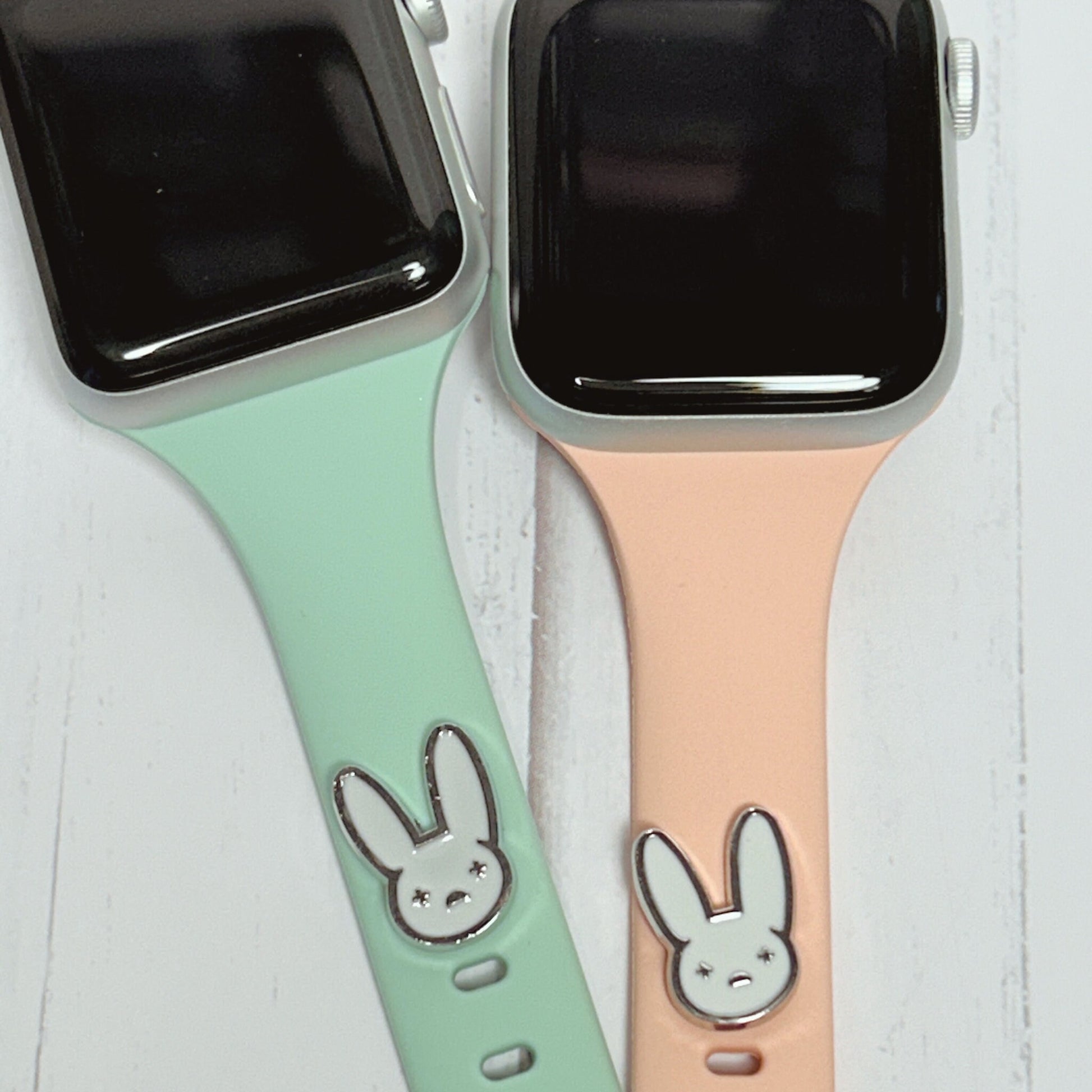 May include: Two Apple Watch bands, one is mint green and the other is peach. Both bands have a silver bunny rabbit charm attached.