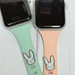 May include: Two Apple Watch bands, one is mint green and the other is peach. Both bands have a silver bunny rabbit charm attached.