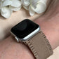 May include: A silver Apple Watch with a brown woven band. The watch face is black and the band has a textured design.