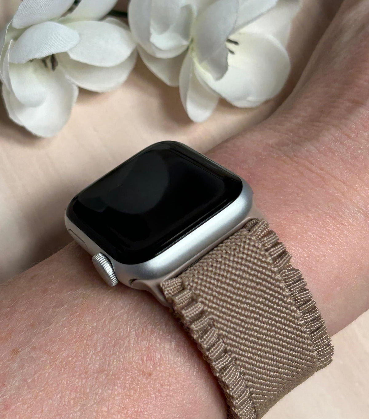 May include: A silver Apple Watch with a brown woven band. The watch face is black and the band has a textured design.